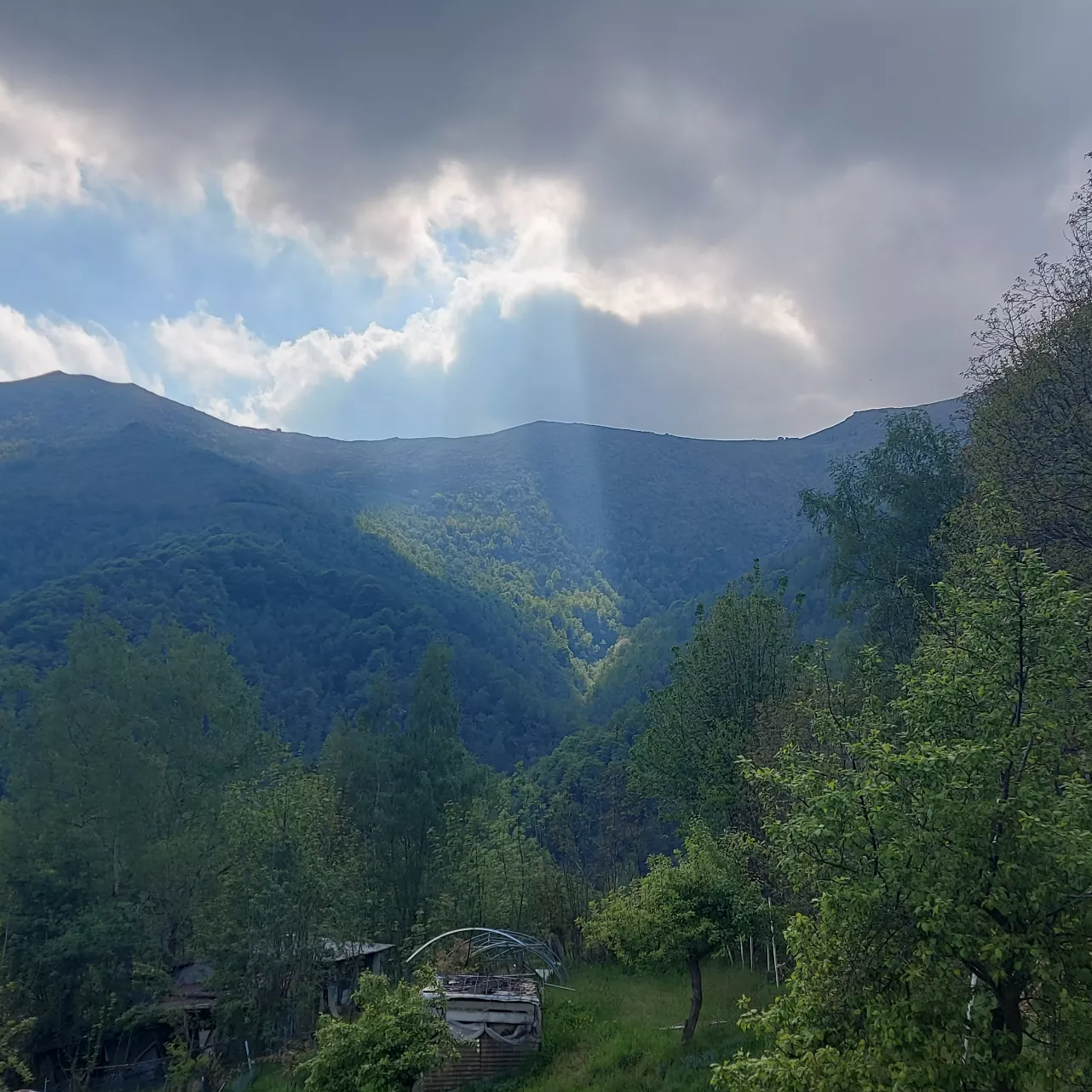 Sonnenstrahlen durchbrechen eine dichte Wolkendecke über einer hügeligen Landschaft